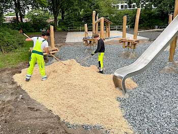 Guned und Luca verteilen das Fallschutzmaterial Öcocolor im Fallbereich des neuen Spielgerätes. (Foto: Ausbildungsbetrieb Gartenbau der Stadt Hannover)